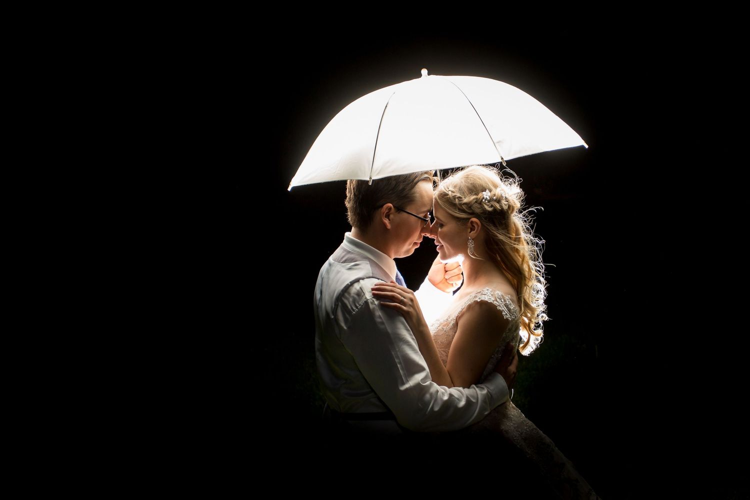 Couple sharing intimate moment under white umbrella with dramatic lighting.