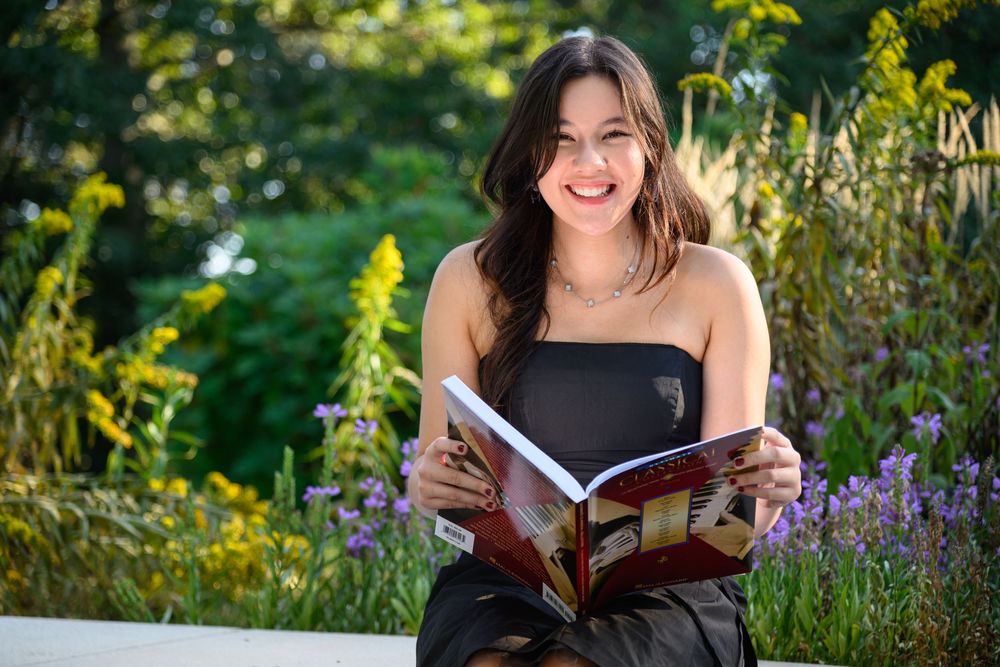 A person reads a book while sitting outdoors among purple wildflowers and lush greenery in natural sunlight.