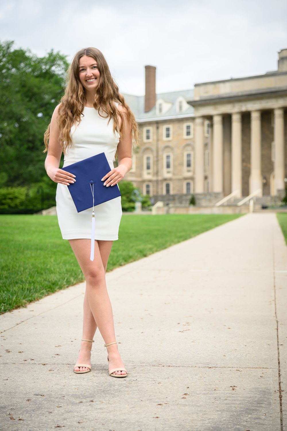 A series of graduation photos showing someone in a white dress and navy stole posing on a college campus walkway.