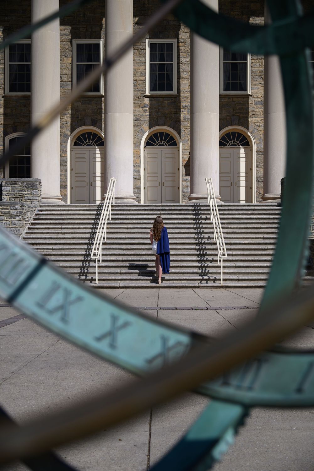 Architectural detail of stone columns and stairs at a university building with a person walking in the distance.