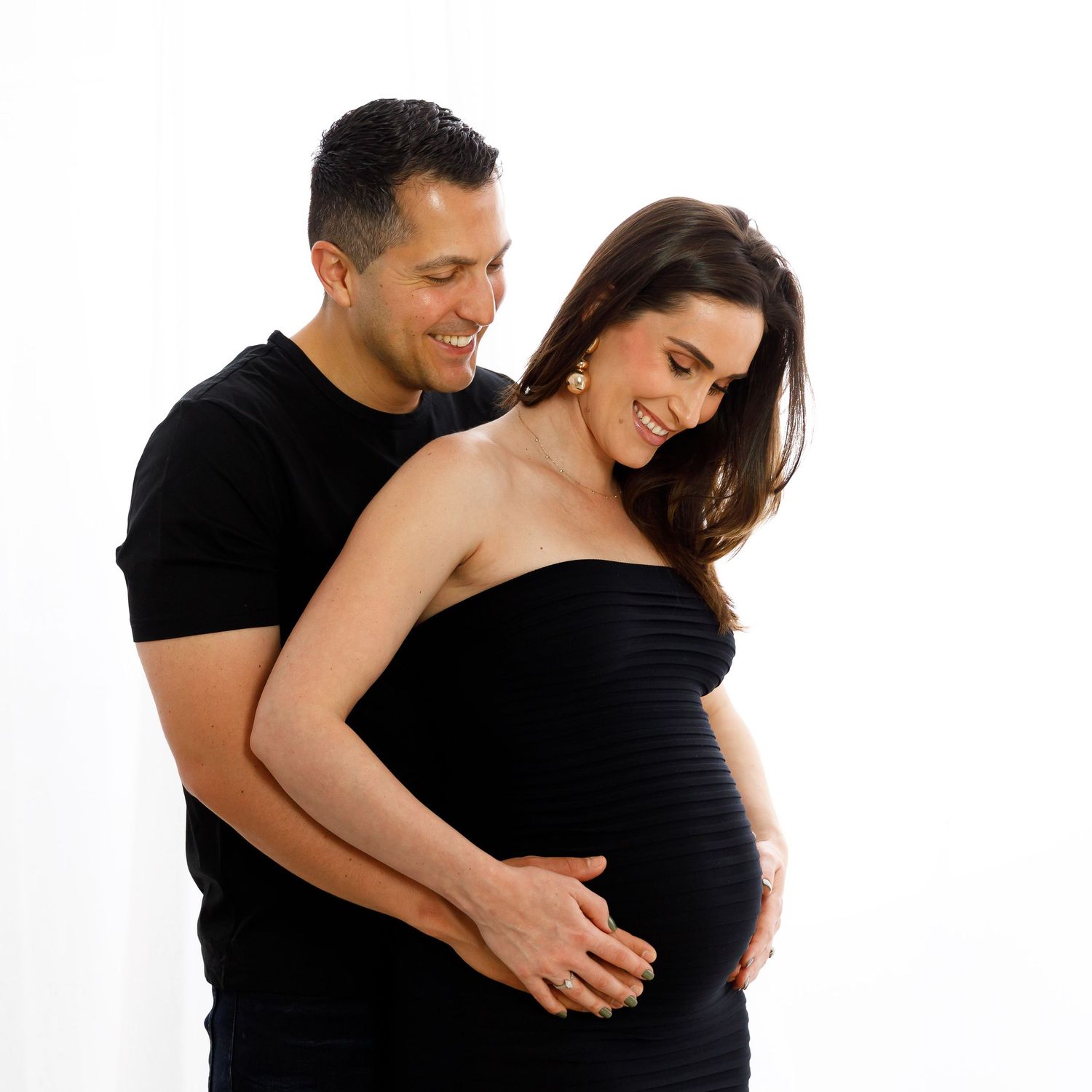 Joyful maternity portrait of couple embracing against white backdrop.