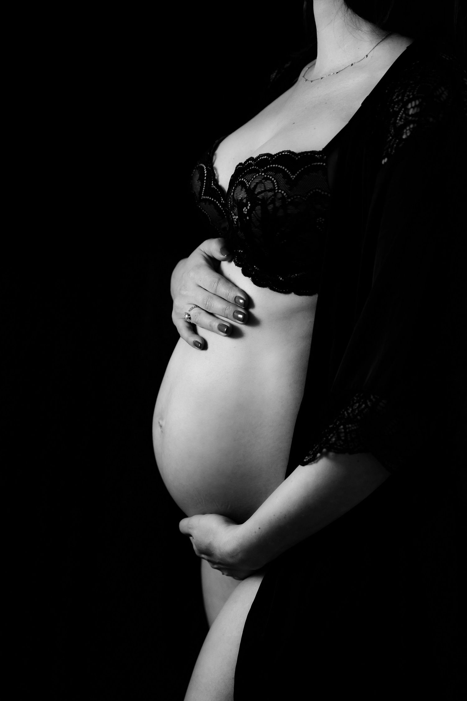 Black and white artistic close-up of pregnant belly with lace details.