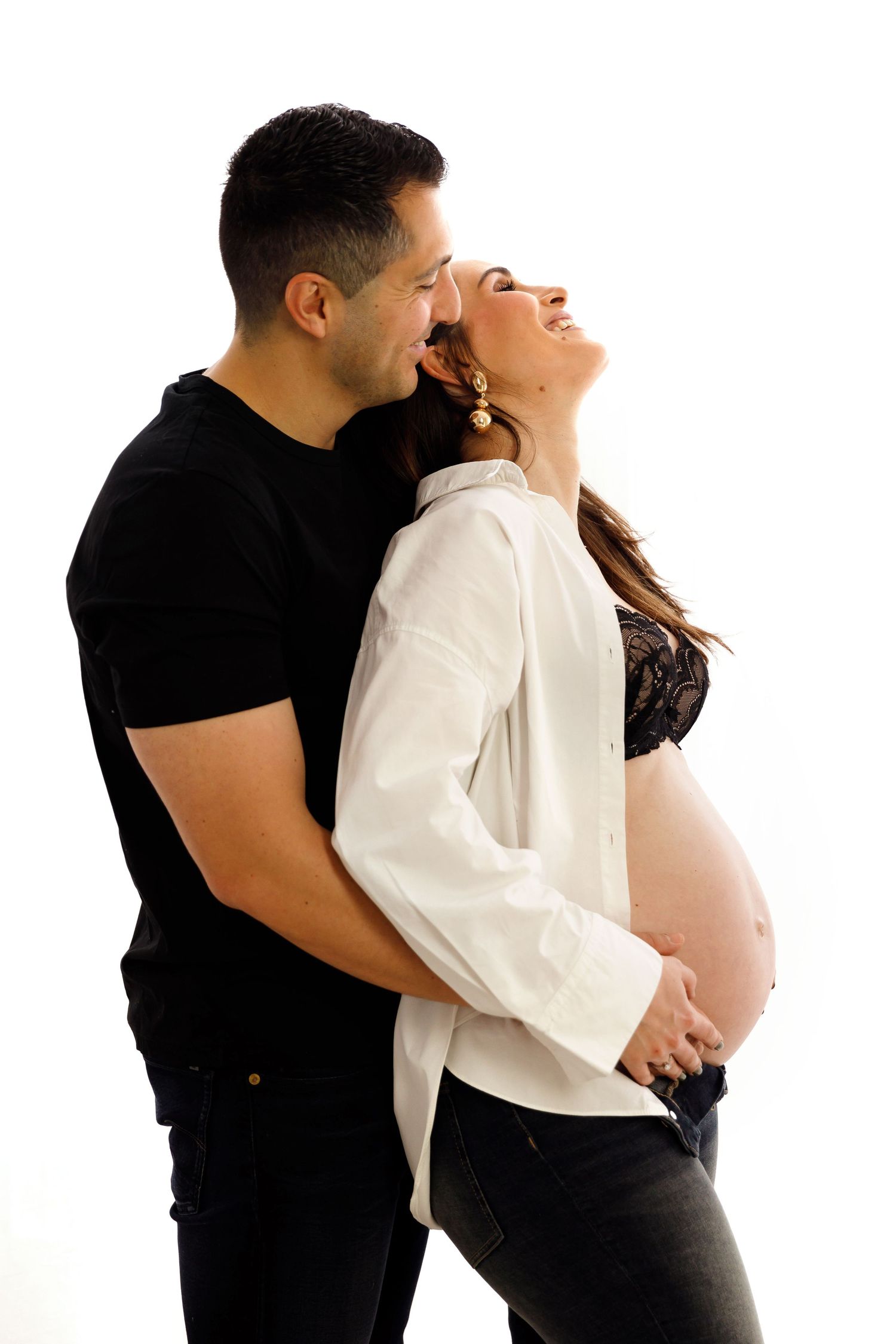 Intimate maternity portrait of expecting couple embracing against white background.