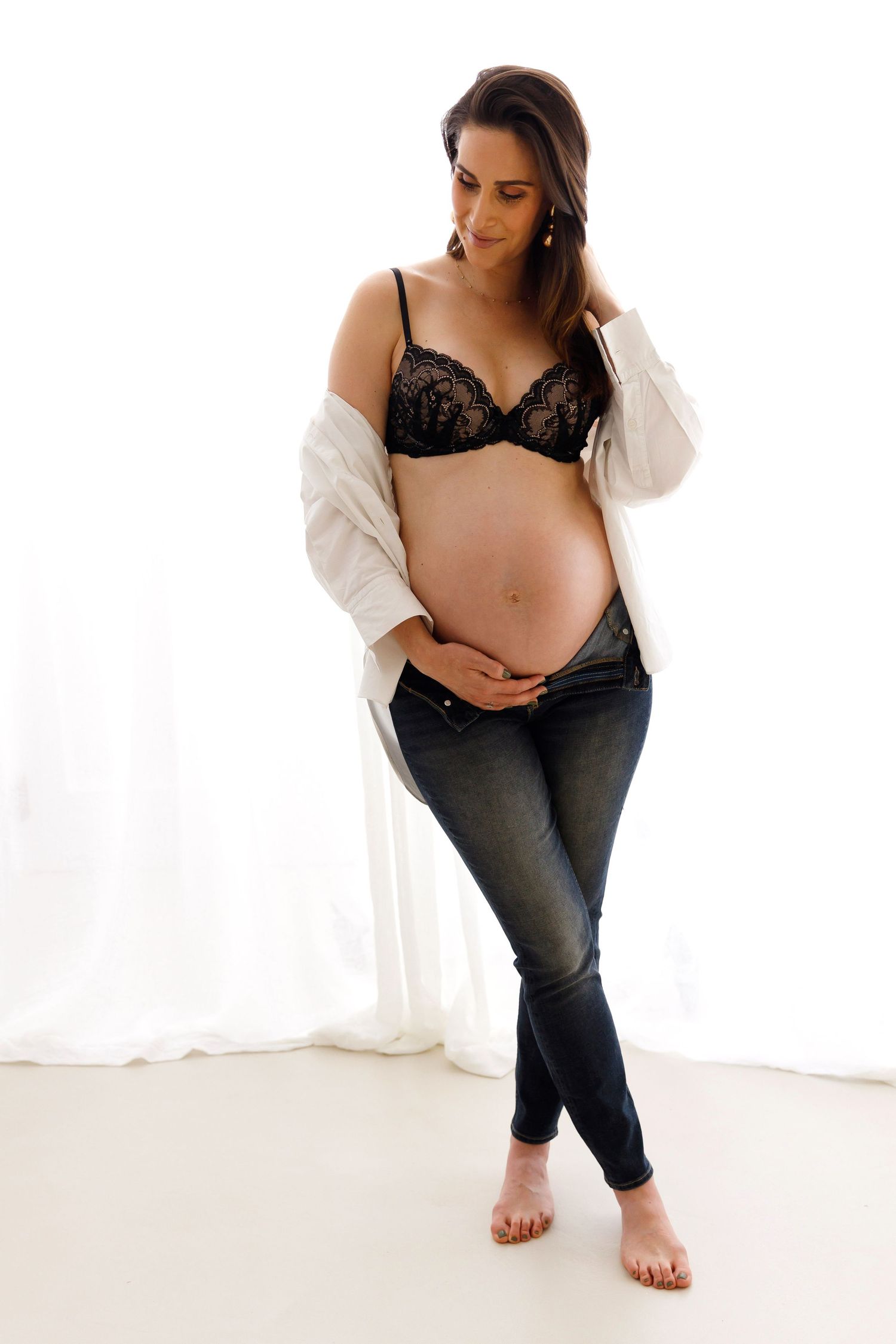 Artistic maternity photo showing pregnant figure in white cardigan and jeans against white backdrop.
