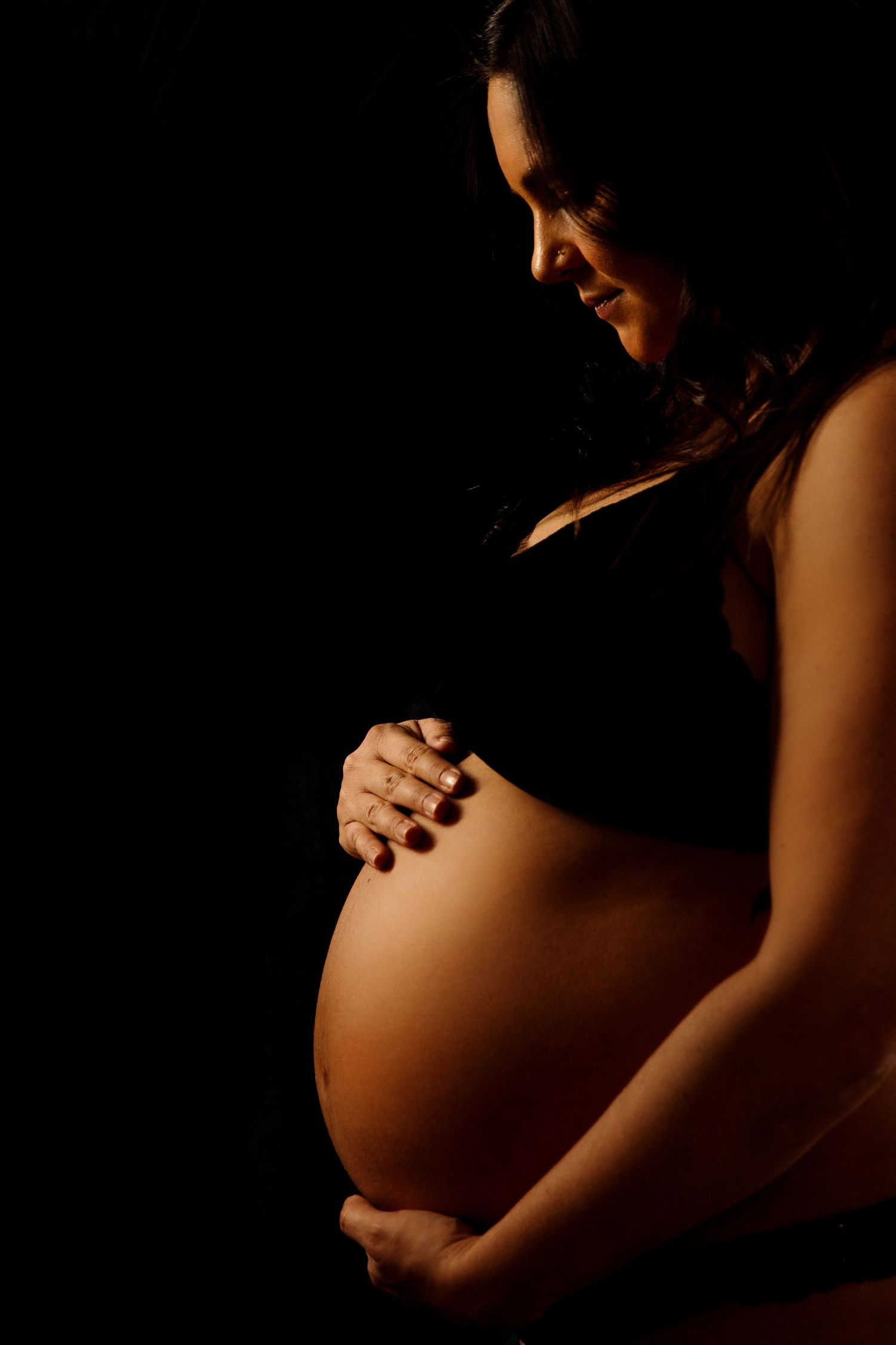 Dramatic side-lit maternity silhouette against black background.