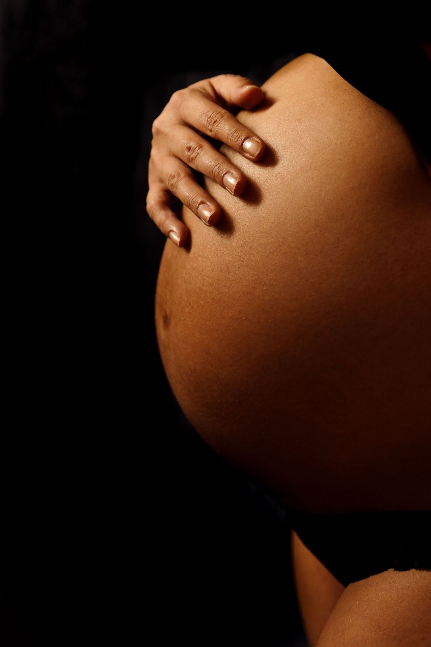 Artistic close-up of hands cradling pregnant belly in warm lighting.