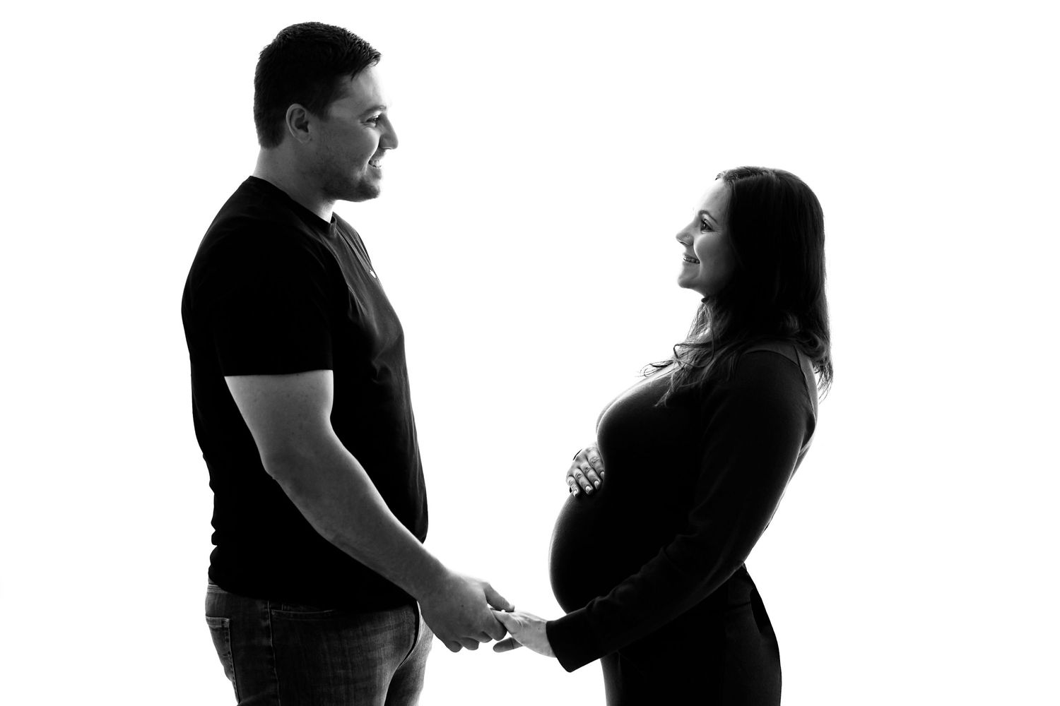 Silhouette of couple holding hands in tender maternity moment against white background.