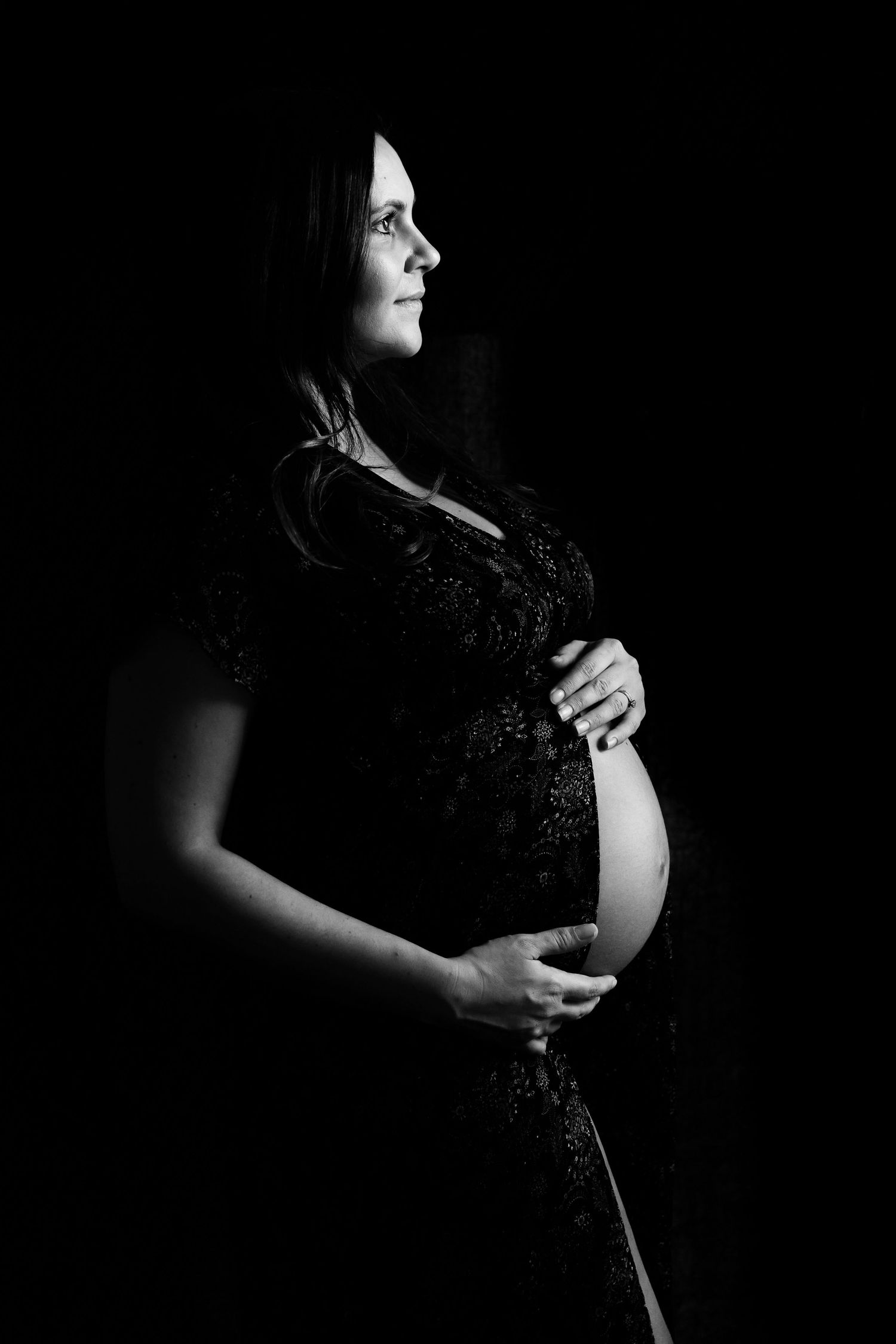 Dramatic black and white maternity silhouette showing pregnant belly against dark background.