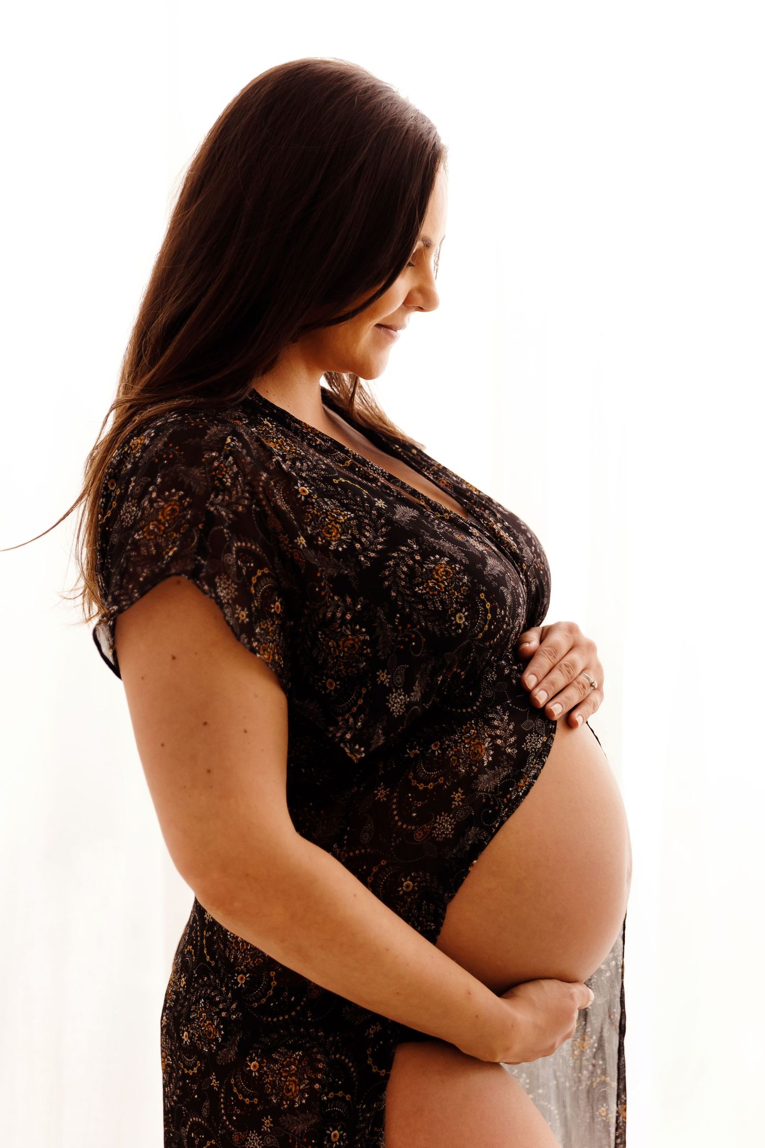 Artistic maternity portrait of an expectant mother in black lace against white background.