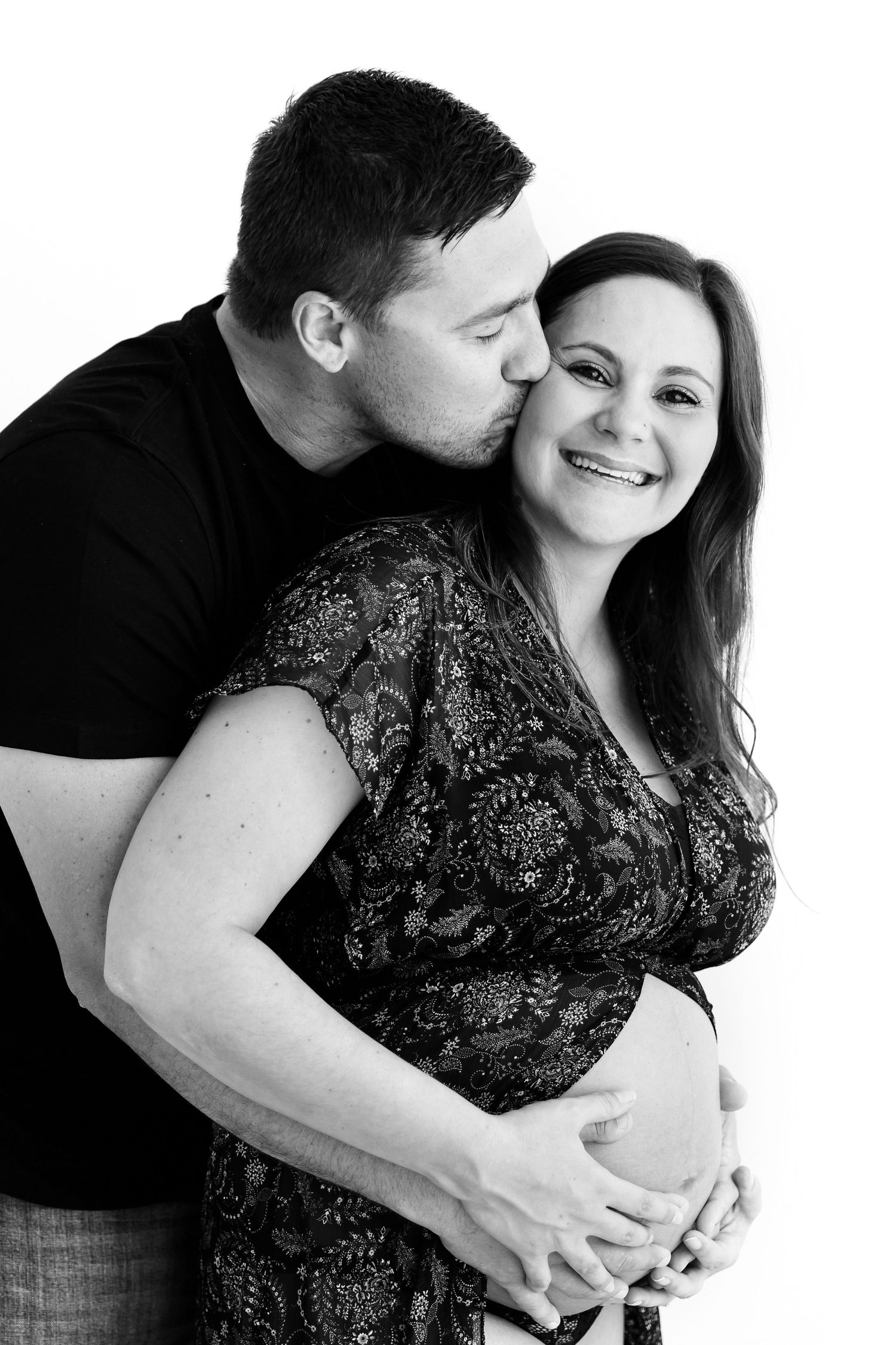 Black and white portrait of couple sharing intimate moment during maternity photoshoot.