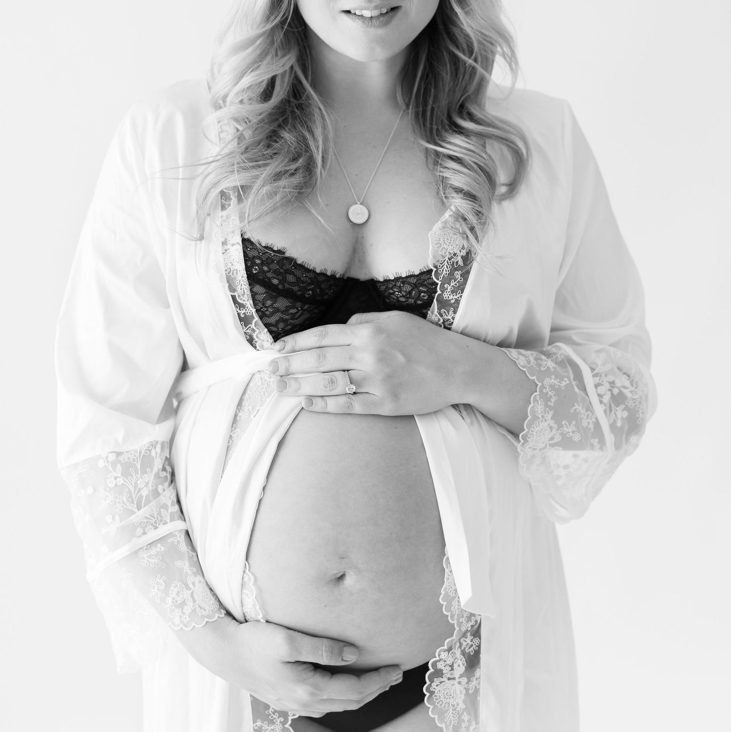 Elegant maternity boudoir photo with white lace robe and black undergarments.