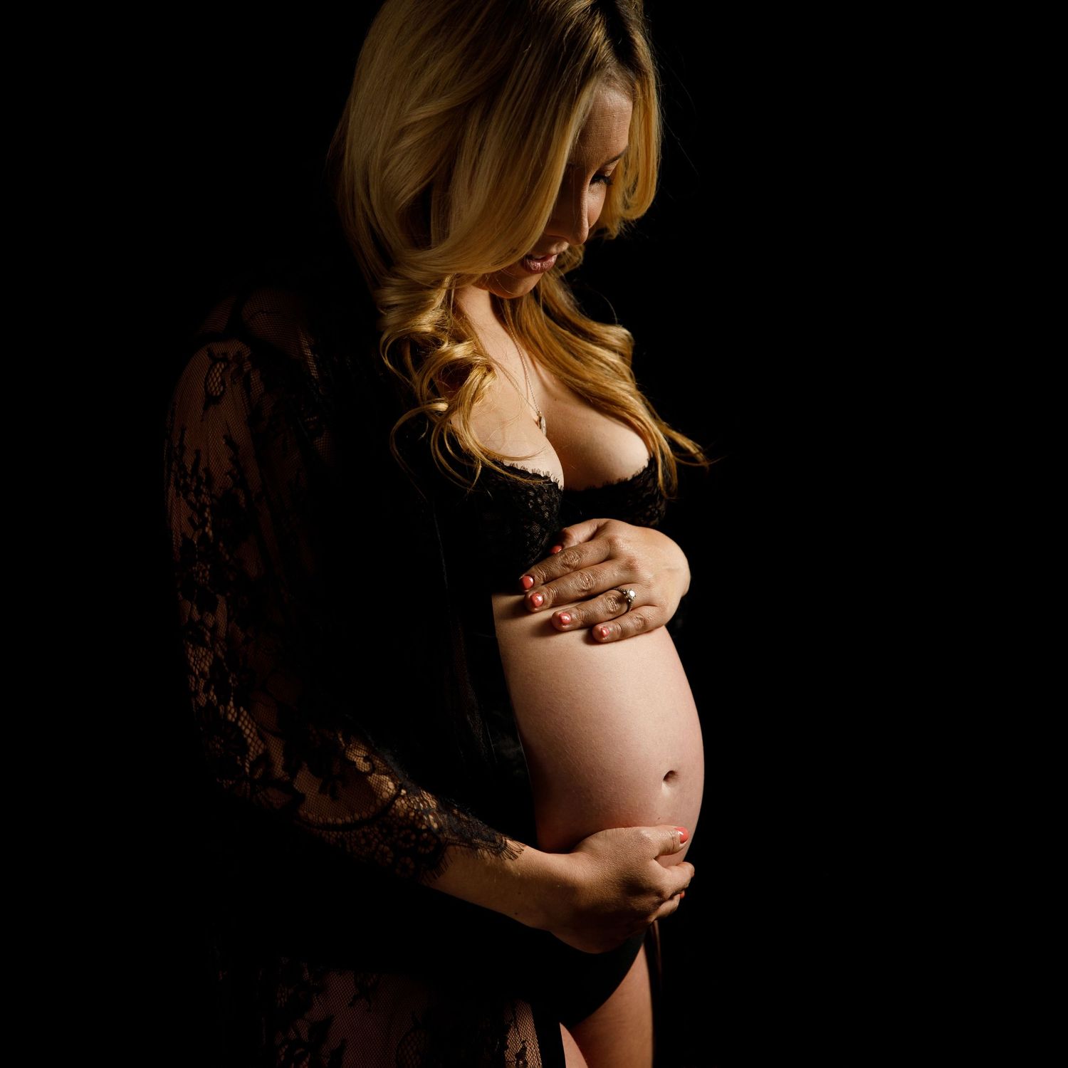 Artistic maternity photo showing a pregnant silhouette in black lace against dark background.