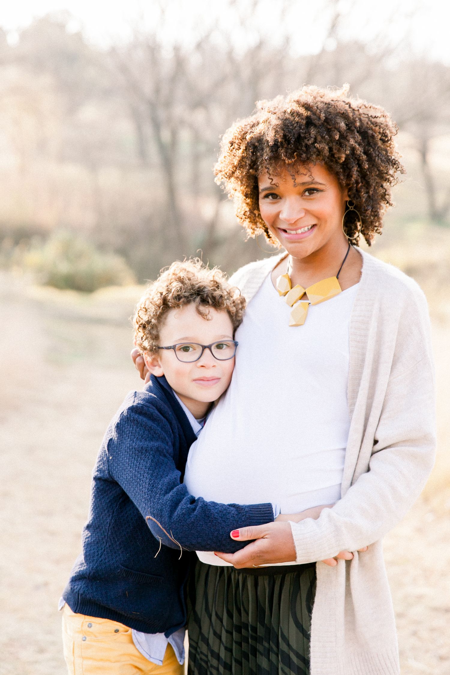 Heart-warming outdoor family maternity photo with child hugging mother's belly.