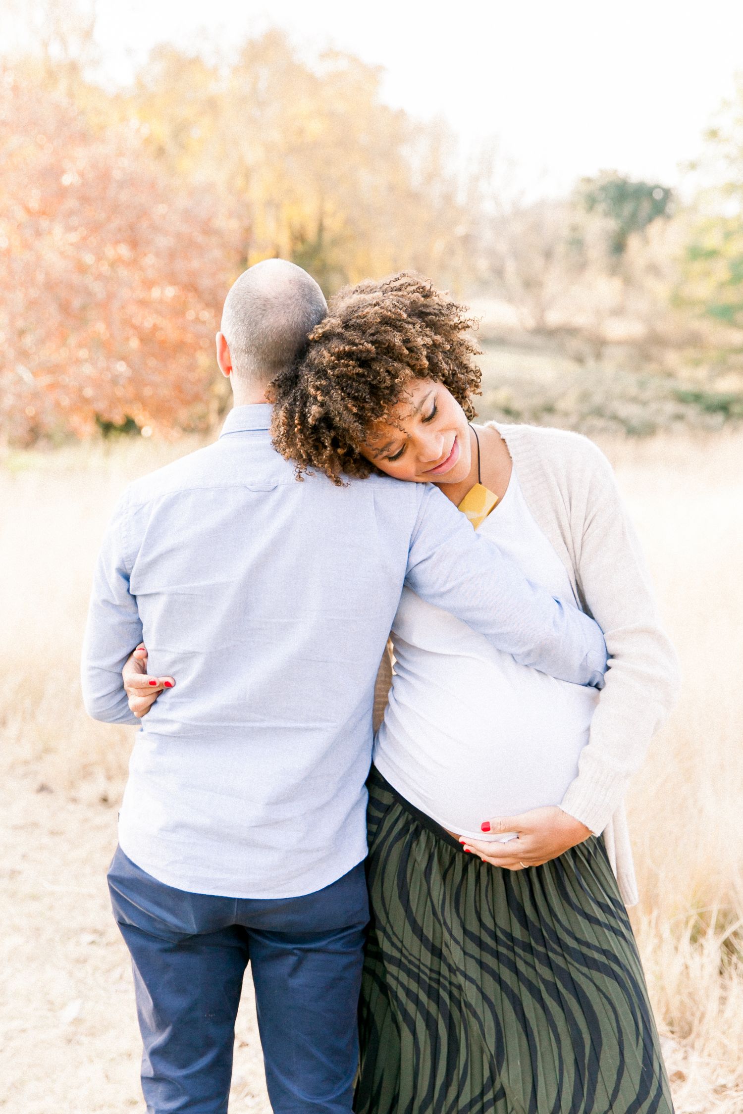 Outdoor maternity photo of couple embracing in golden autumn field.