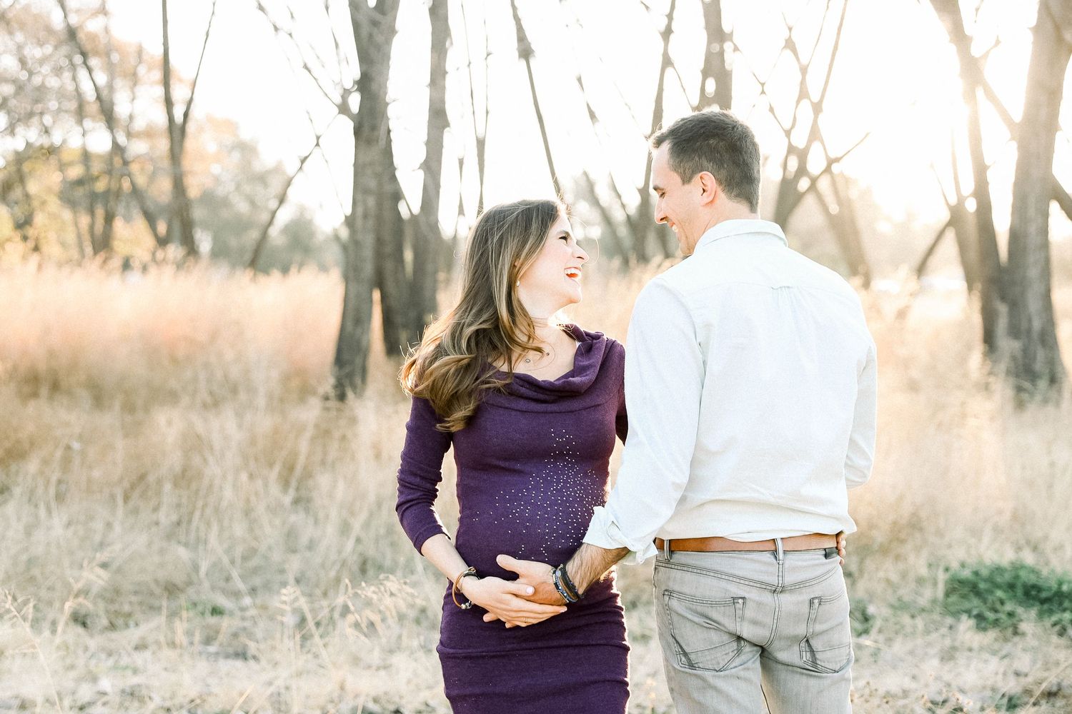 A maternity photoshoot featuring a purple dress in a scenic outdoor setting with golden sunlight.