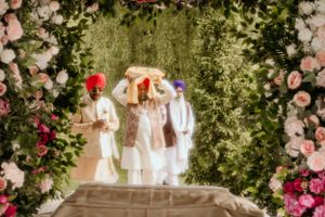 Wedding ceremony setup with floral archway and pink roses against green foliage.