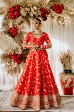 A stunning red bridal lehenga with intricate embroidery and floral arch decor in beige and red tones.