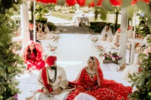 Traditional Sikh wedding ceremony with red and white decor in outdoor garden setting.