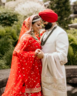 Wedding couple in traditional Sikh attire share a tender moment in an outdoor garden setting.