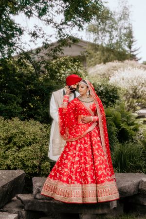 Romantic outdoor wedding portrait with couple in red and white traditional Indian attire.