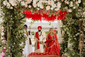 Sikh wedding ceremony taking place under an elaborate floral mandap with white roses.