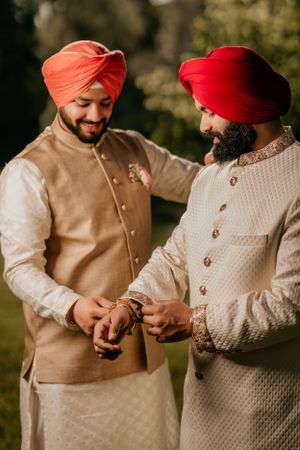 Two men in traditional Indian attire and turbans share a moment during wedding celebrations.