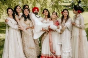 Wedding party in white and cream outfits poses with couple in traditional Sikh attire.
