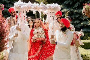 Sikh wedding ceremony under white floral canopy with traditional attire of red and white.