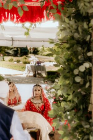 Traditional wedding ceremony framed by greenery and red decorations in an outdoor garden setting.