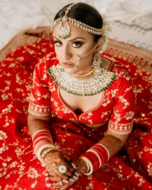 Traditional Indian bride in red lehenga adorned with intricate jewelry and bridal accessories.