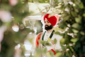 Artistic wedding portrait through foliage of groom in traditional Sikh attire.