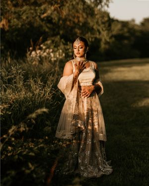 Golden hour portrait of person in sparkly champagne-colored South Asian formal attire in garden setting.