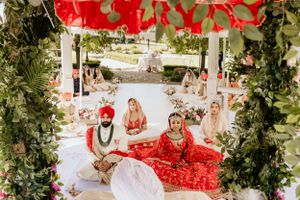 Traditional Indian wedding ceremony taking place under a decorated mandap with red and white floral arrangements.