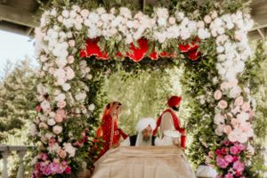 Floral wedding arch decorated with white roses and red accents for an outdoor ceremony.
