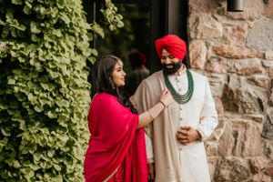 Couple in traditional Indian wedding attire standing by stone wall with climbing vines.