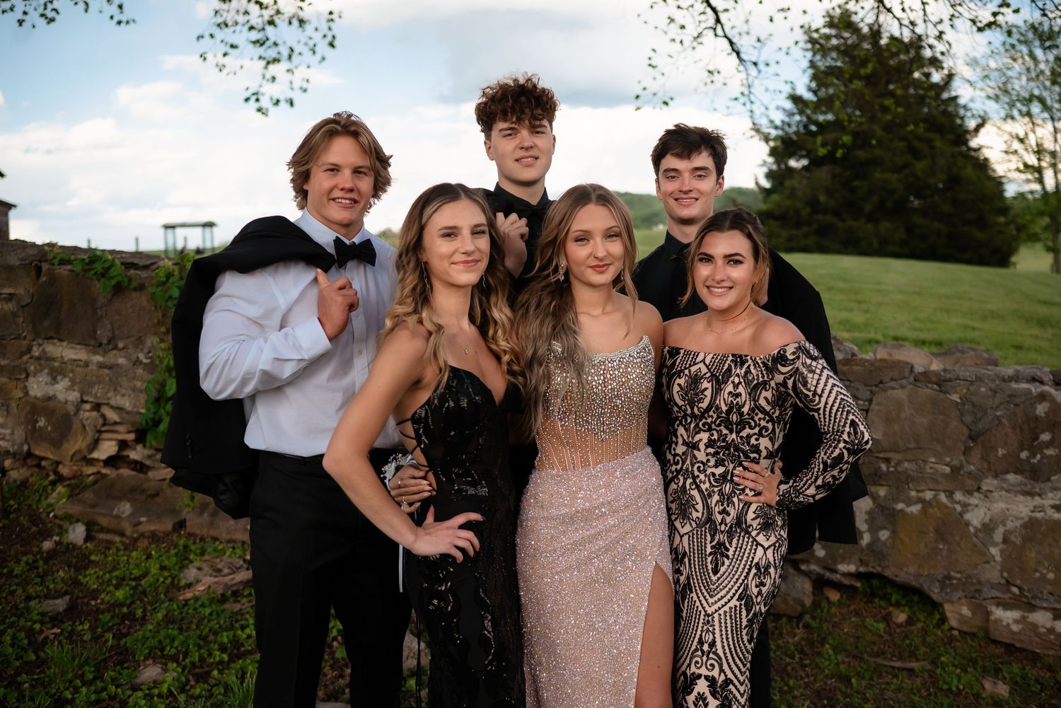 Formal group photos taken outdoors with people wearing elegant dresses and suits for a special occasion.