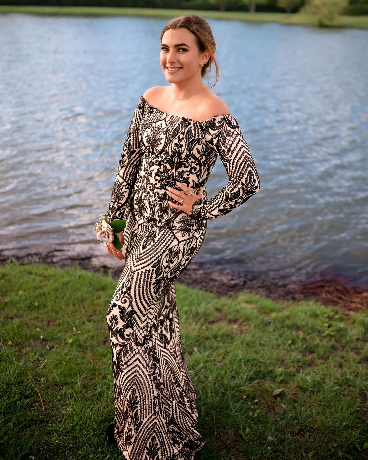 Person wearing patterned black and white dress poses near waterfront during golden hour.