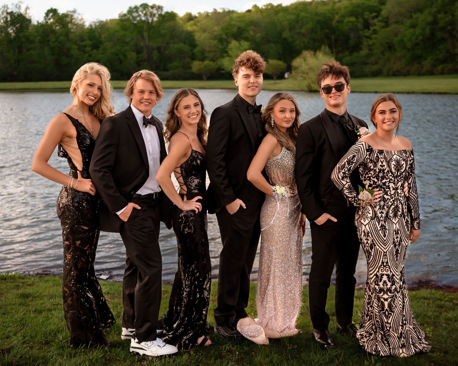 A group in formal attire poses together by a lake for a celebratory photo.