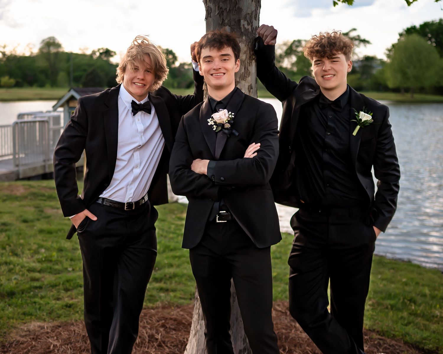 A group of formally dressed people pose playfully together outdoors near water.
