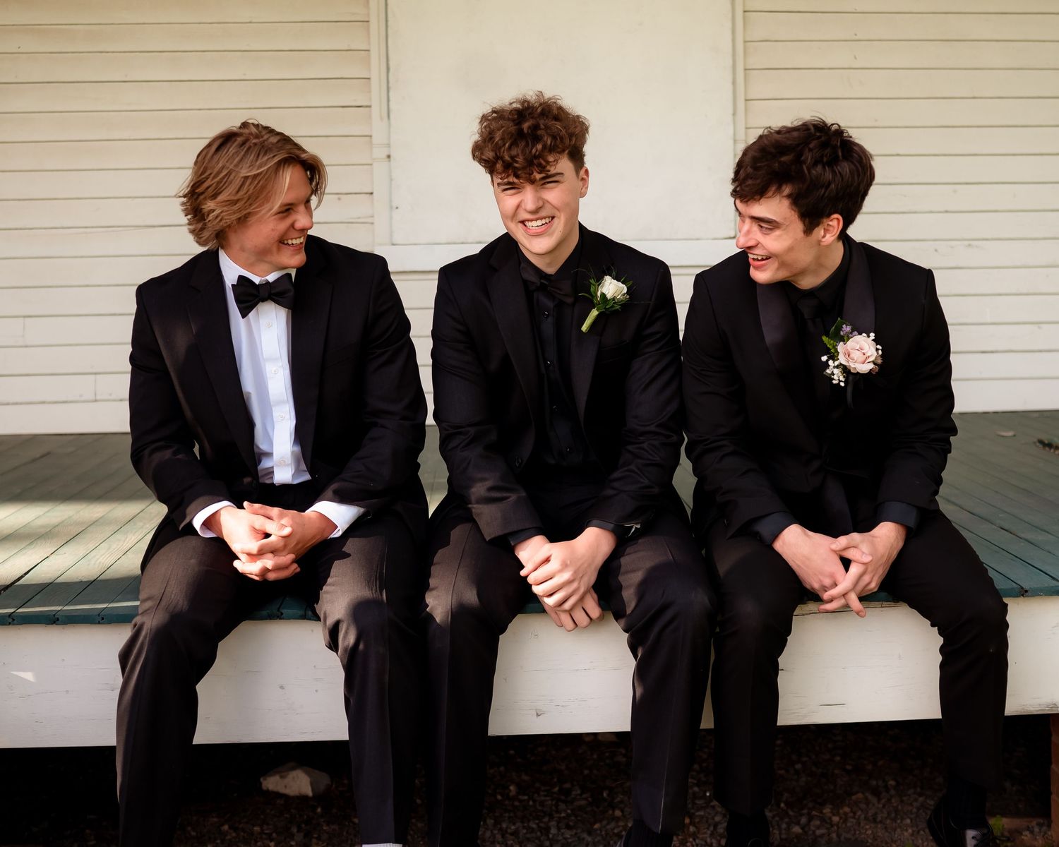 Young men in black tuxedos sitting together on porch steps.
