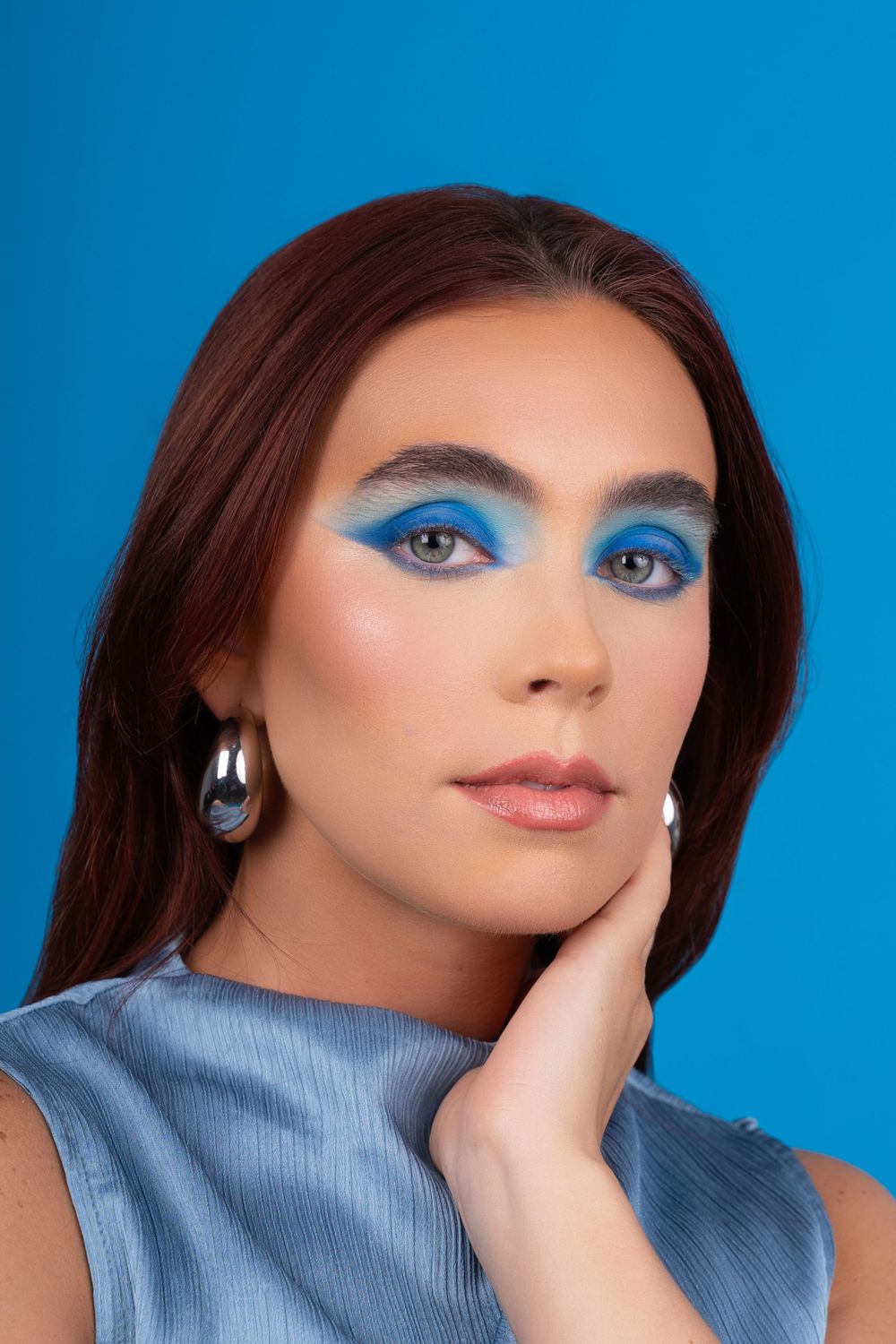 Beauty portrait of a woman with bold makeup against a blue background.