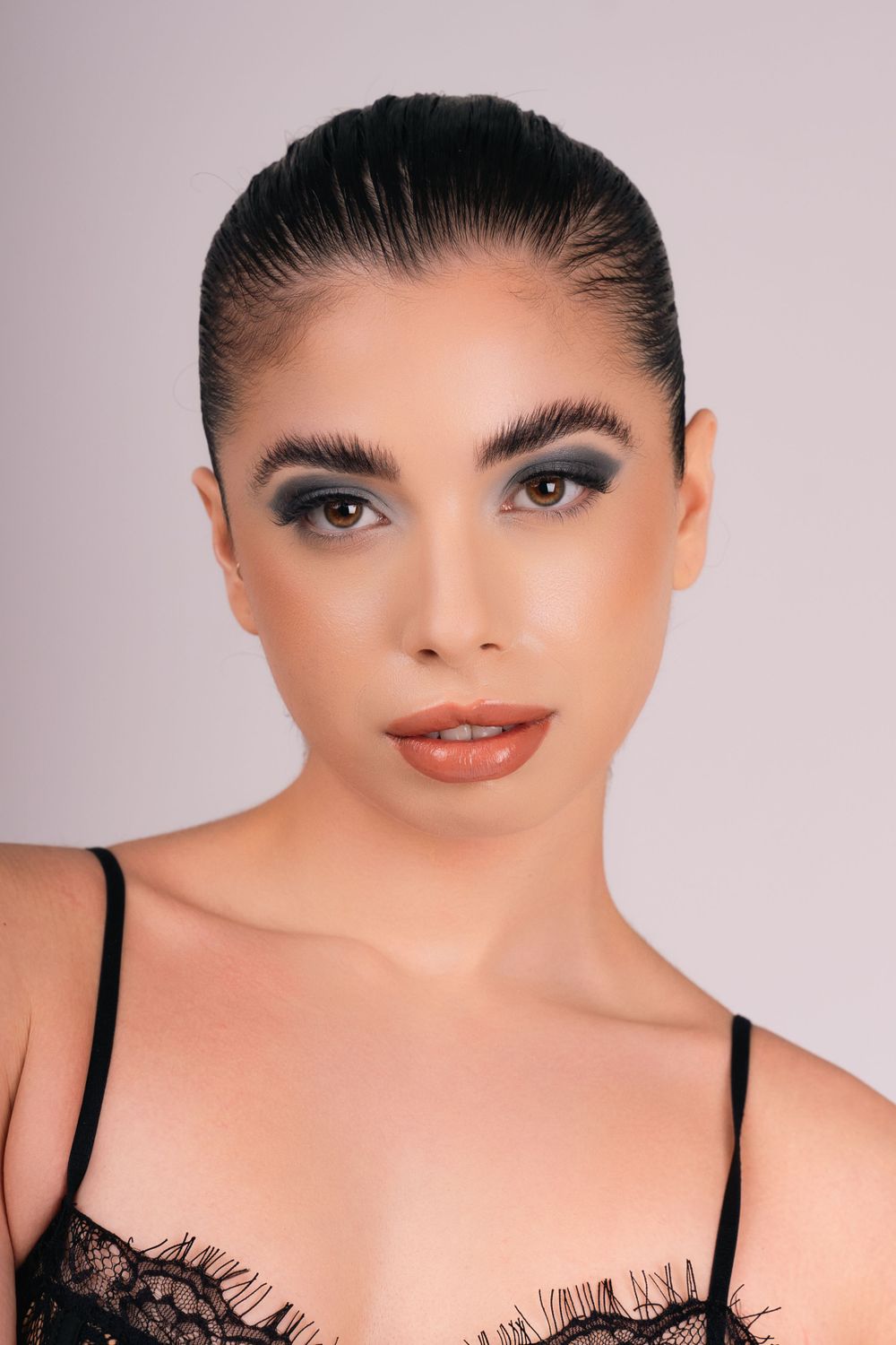 Studio beauty photo of woman with slicked-back hair and smoky shadow, wearing a black lace top in New York.