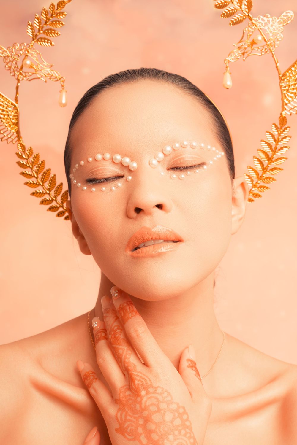 Surreal editorial with pearl makeup and henna hand art, orange background – NYC conceptual shoot.