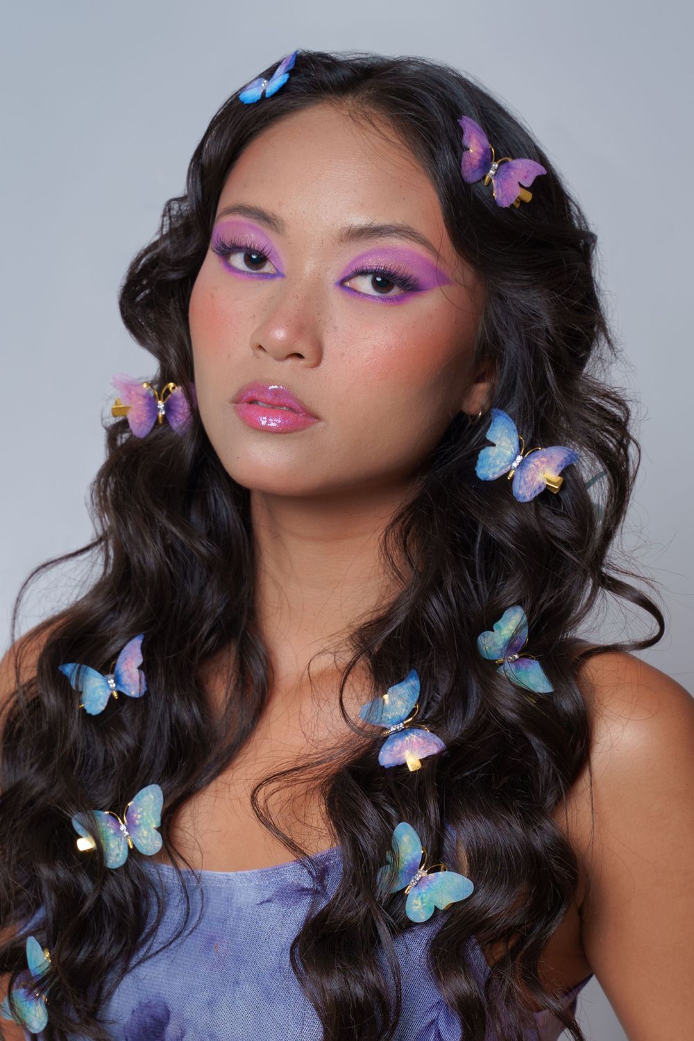 Model with butterfly hair clips, glossy lips, and purple eyeshadow in whimsical NYC studio shoot.