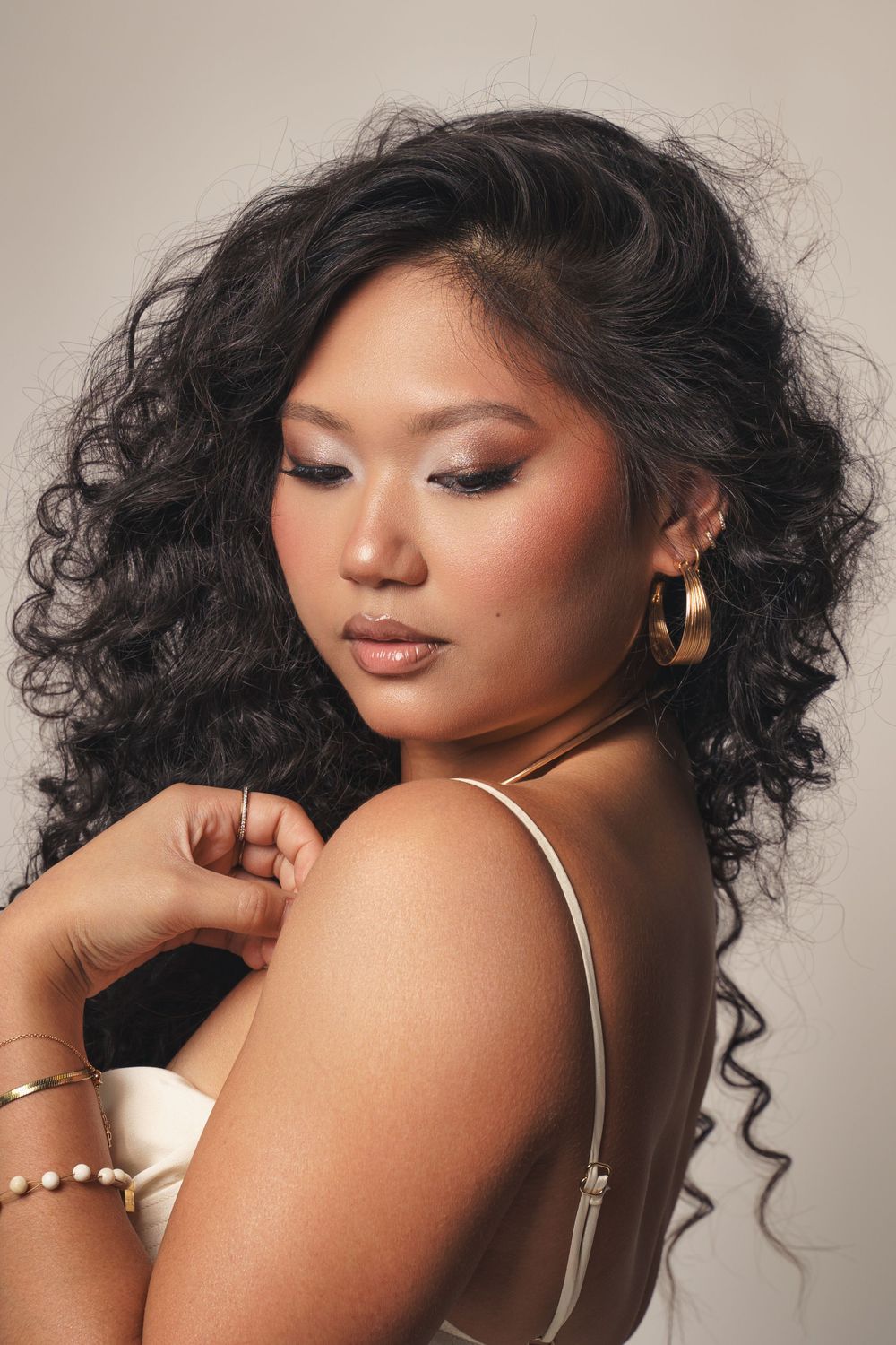 Natural glam portrait of curly-haired woman with gold jewelry, neutral tones, and soft light – shot in NYC.