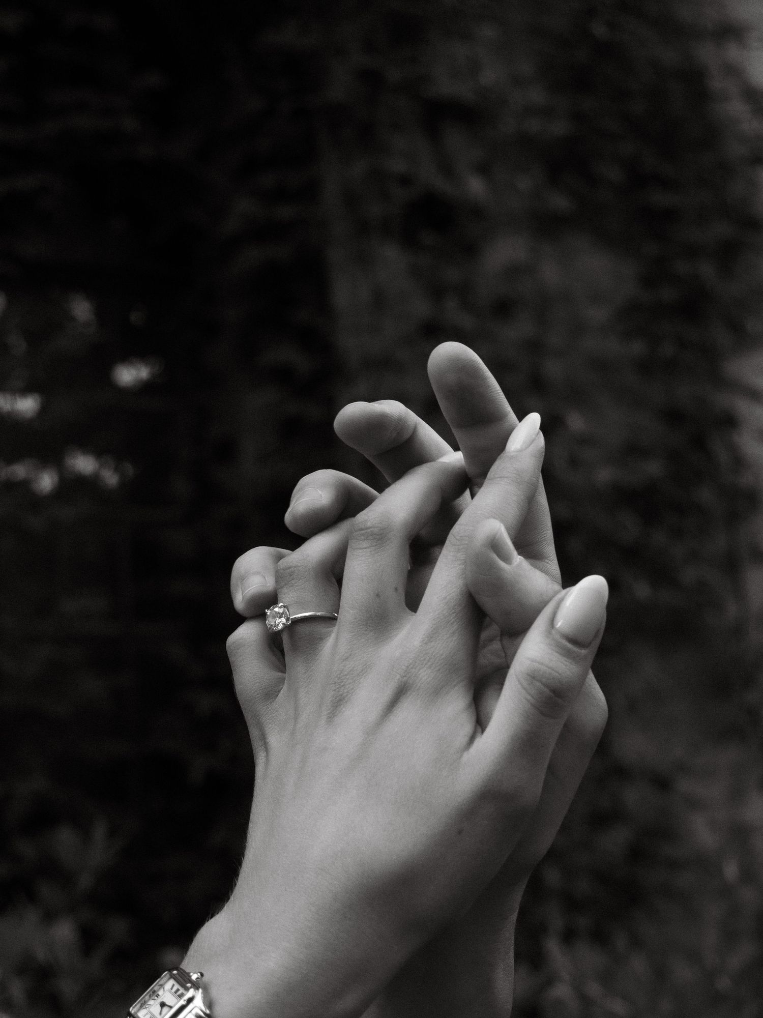 Two hands with wedding rings intertwined in a tender embrace against a dark background.