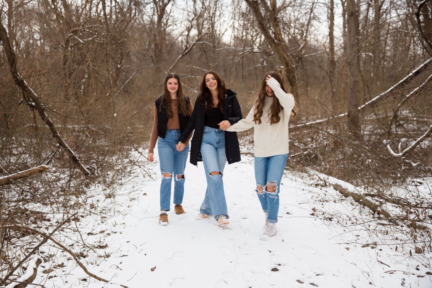 Three friends walking together through a snowy forest path wearing coordinated winter outfits.