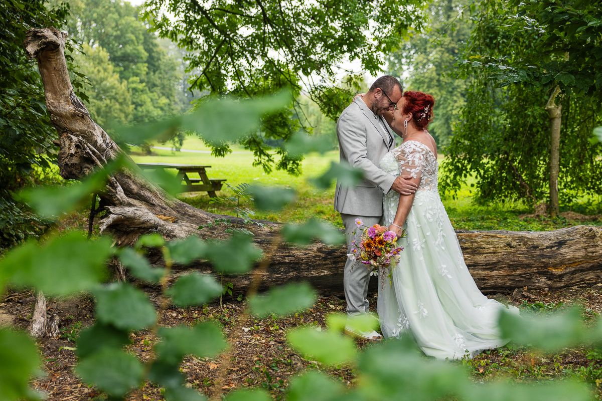 A wedding couple shares an intimate moment in a lush garden setting with a dreamy green backdrop.