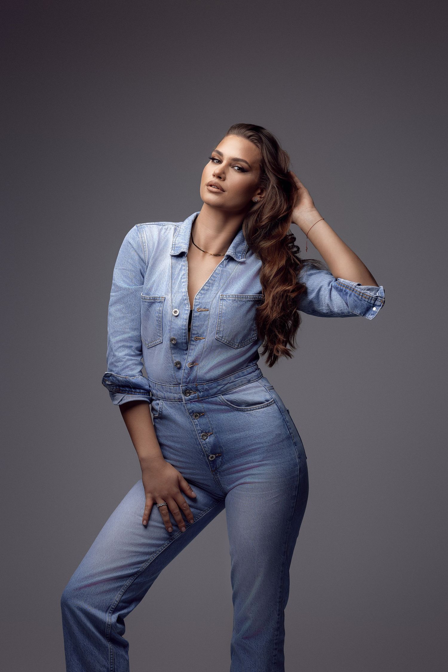 Model in all-denim ensemble poses dramatically on grey backdrop.