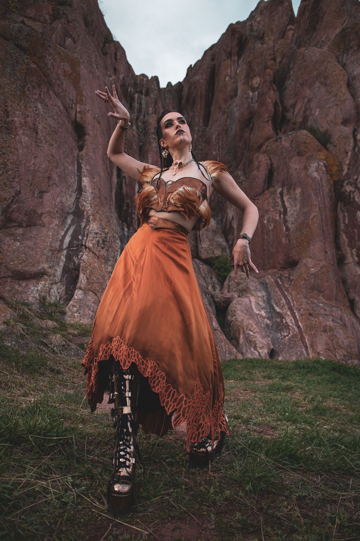 Dramatic fashion pose in orange flowing dress against red rock canyon formations.